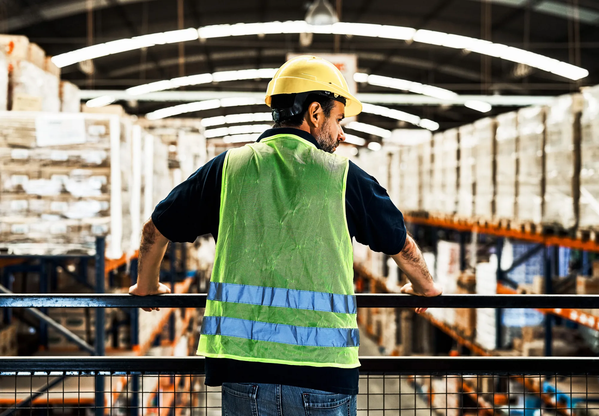 Worker standing on an elevated walkway looking at the warehouse floor. Original File